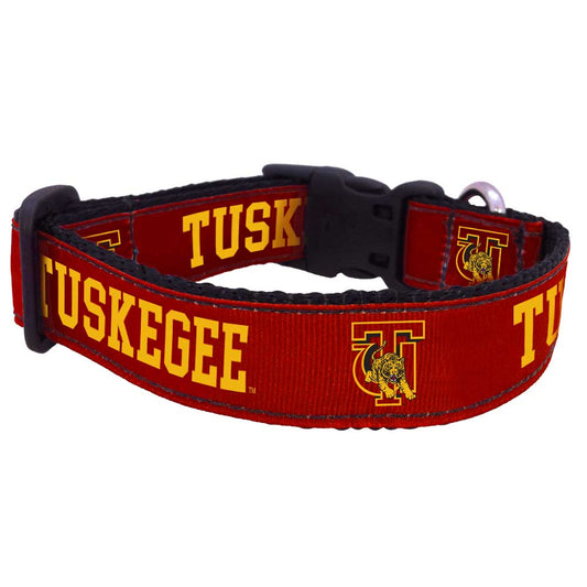 A red pet collar with 'TUSKEGEE' printed in bold letters along its length, featuring a university logo on a label.